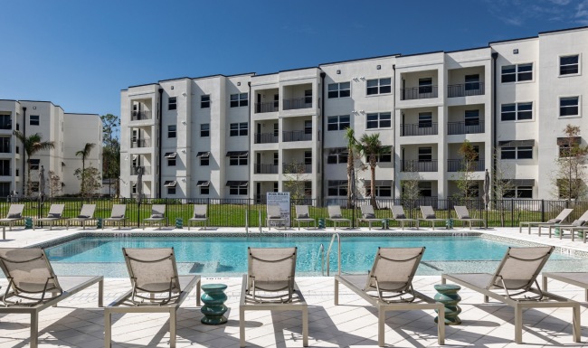 Resort-style swimming pool at Estero Vista in Fort Myers, FL, surrounded by lounge chairs and modern apartment buildings.
